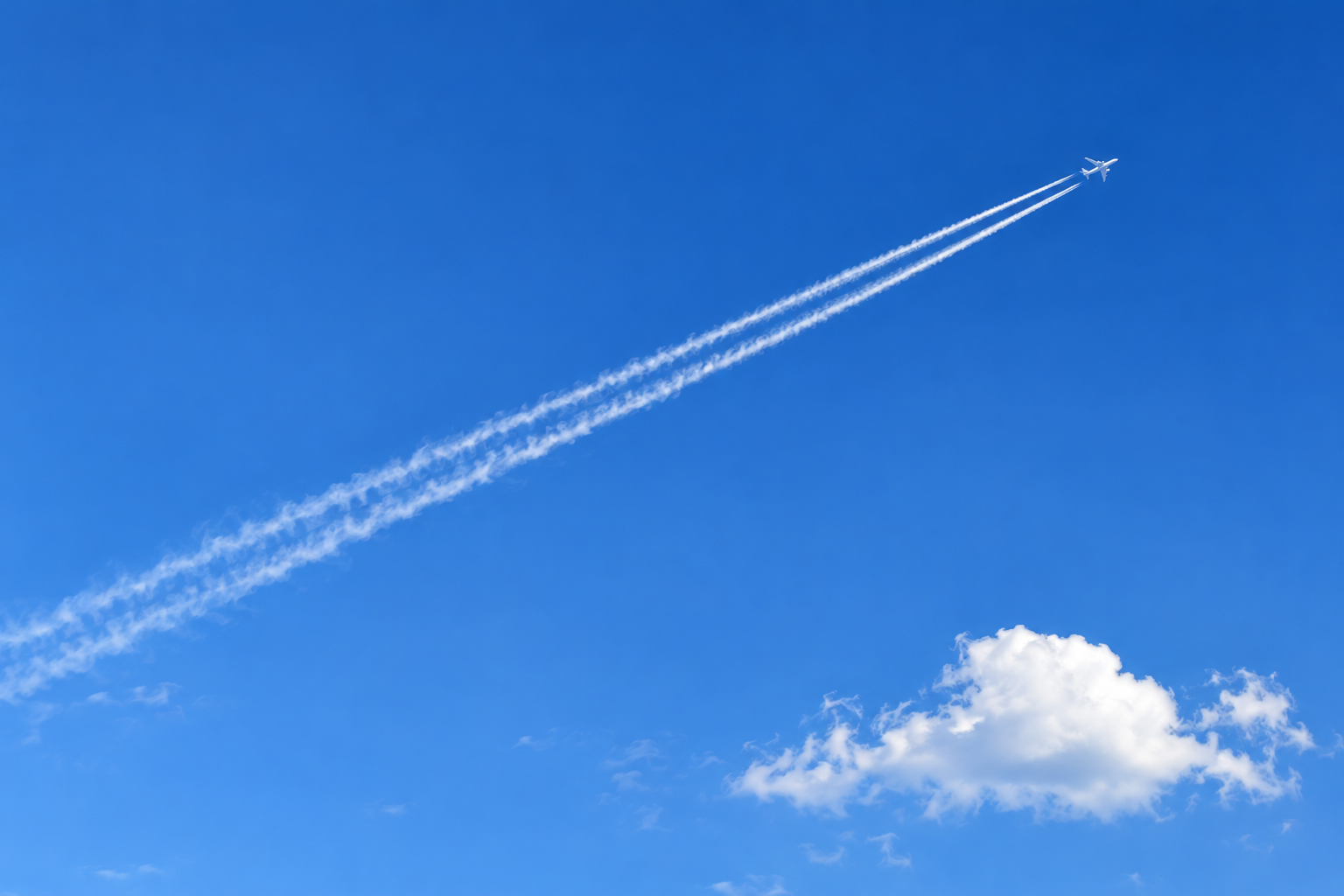 비행기 뒤로 두 갈래 흰 비행운이 길게 이어지는 하늘